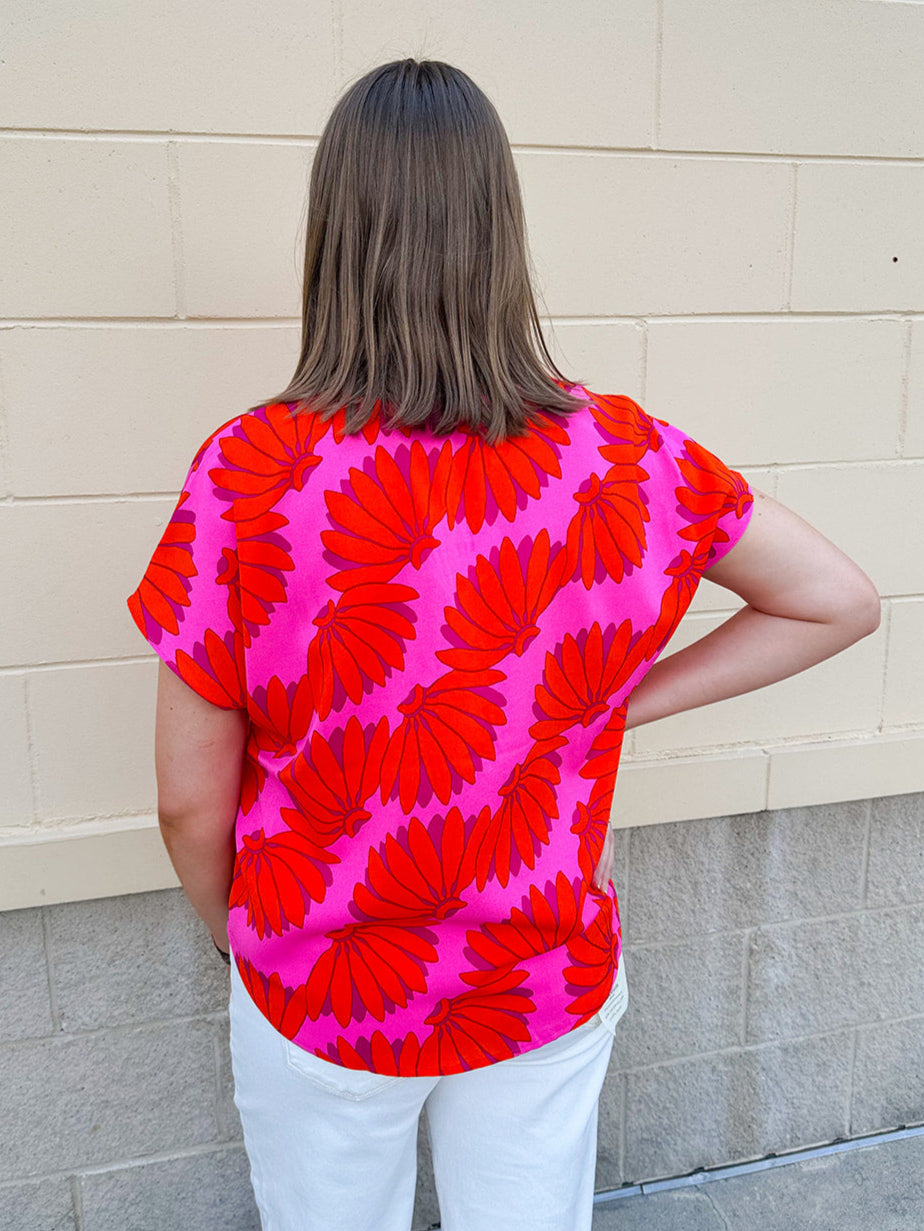 Banana and floral print top in orange and hot pink with V-neck and short dolman sleeves, displayed on hanger against neutral background