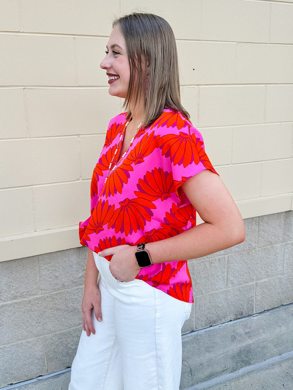 Banana and floral print top in orange and hot pink with V-neck and short dolman sleeves, displayed on hanger against neutral background