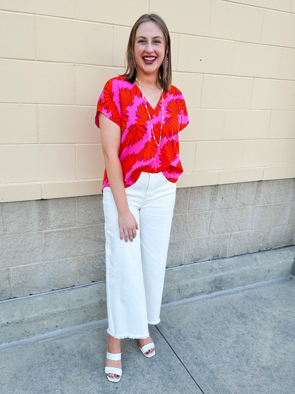 Banana and floral print top in orange and hot pink with V-neck and short dolman sleeves, displayed on hanger against neutral background
