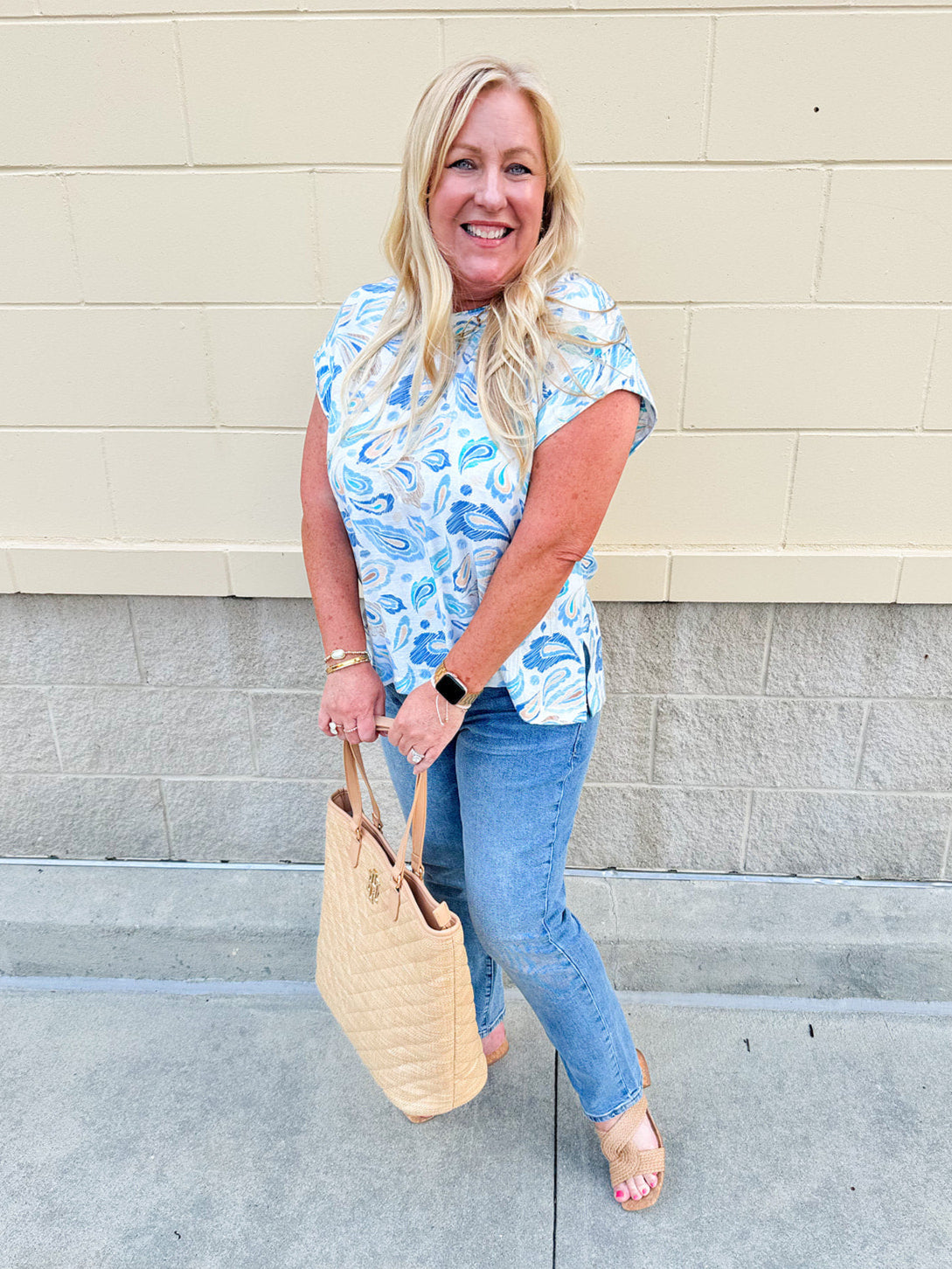 Blue paisley print cap sleeve blouse with round neckline and back button detail, styled for a soft and polished look.