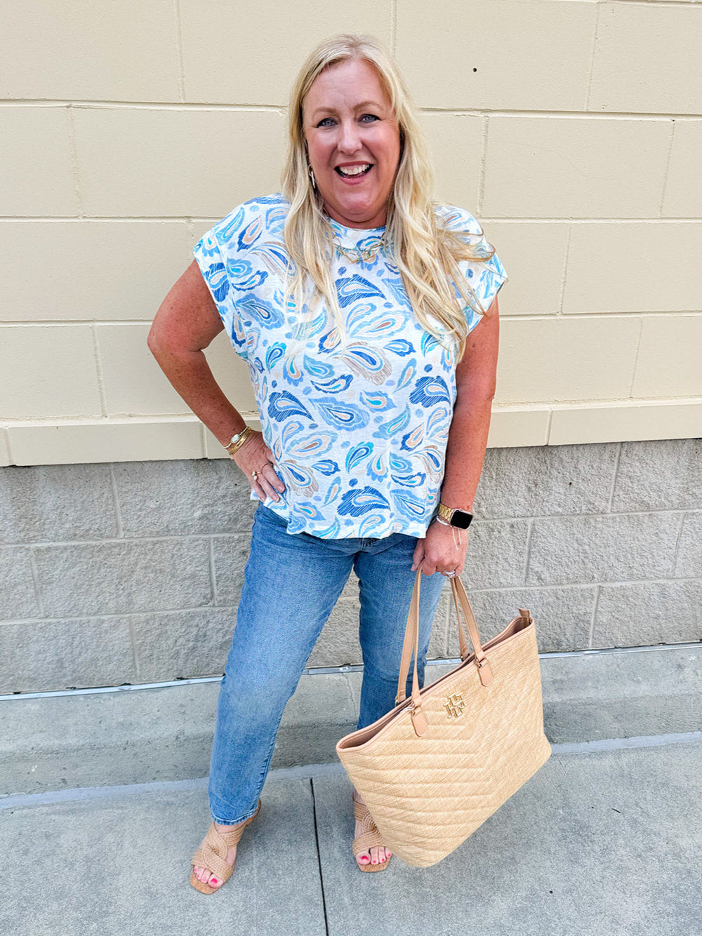 Blue paisley print cap sleeve blouse with round neckline and back button detail, styled for a soft and polished look.