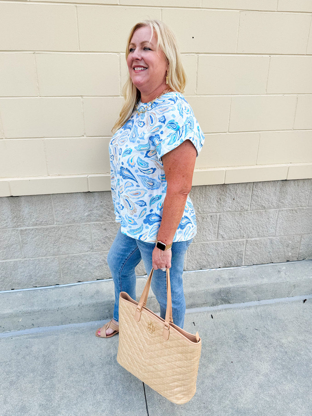 Blue paisley print cap sleeve blouse with round neckline and back button detail, styled for a soft and polished look.