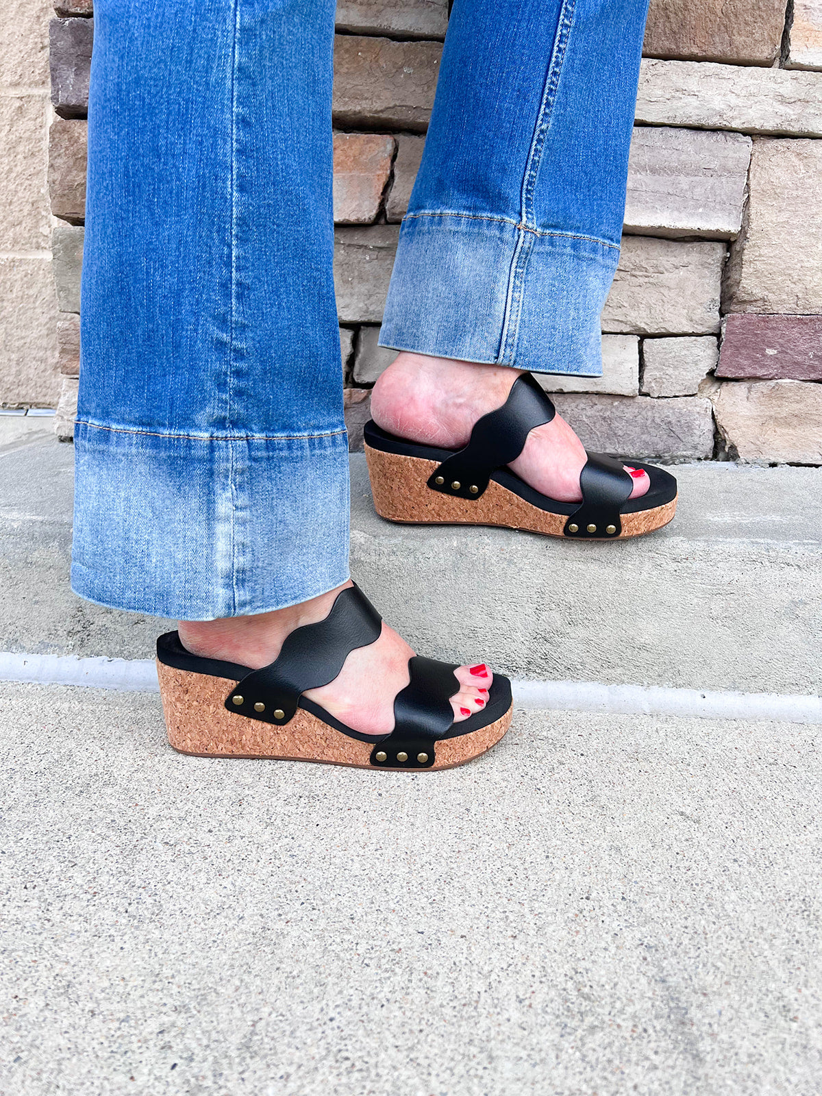 Black scalloped wedge sandals with cork sole, gold hardware accents, and dual straps—stylish and comfortable for everyday wear.