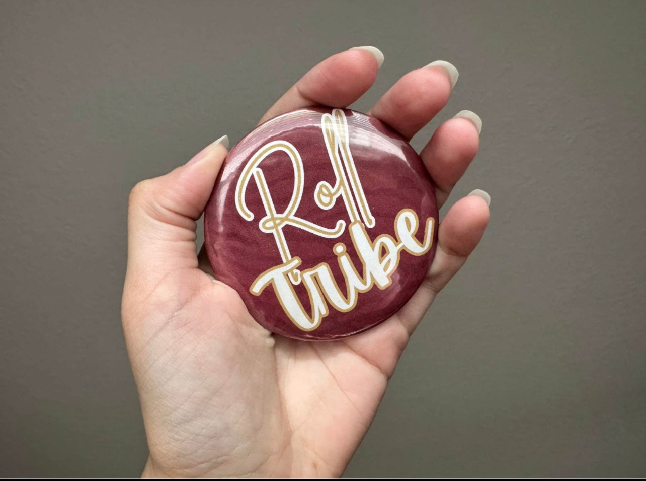 Round garnet & gold button with bold lettering, styled as a gameday accessory on bags, jackets, or outfits.