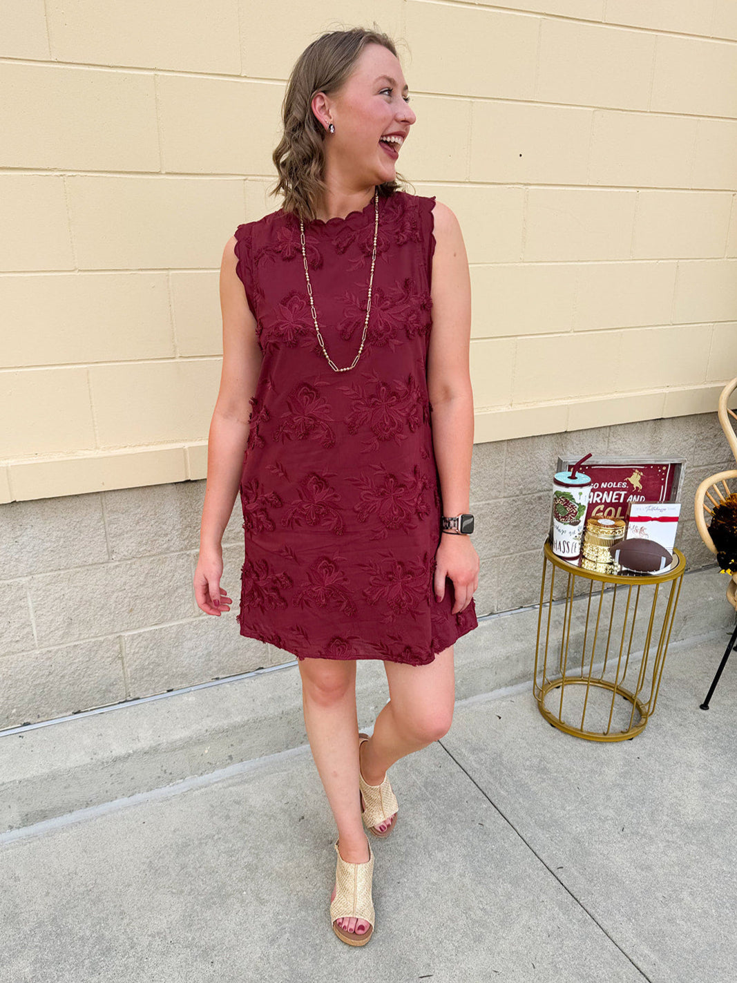 Sleeveless mini dress in rich garnet with 3D floral appliqué, scalloped embroidered hem, and side pockets. Elegant, textured, and perfect for fall or Gameday.