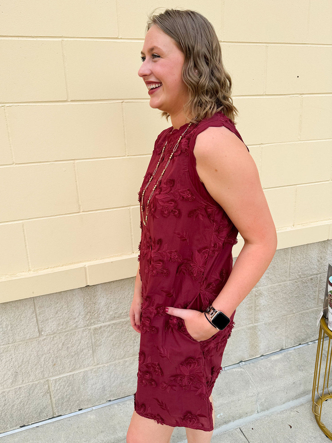 Sleeveless mini dress in rich garnet with 3D floral appliqué, scalloped embroidered hem, and side pockets. Elegant, textured, and perfect for fall or Gameday.