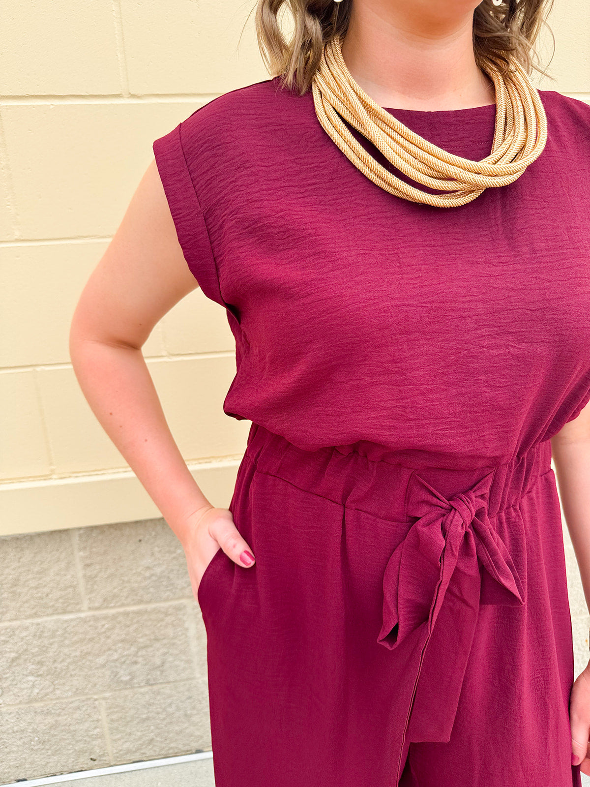 Garnet short-sleeve jumpsuit with elastic waist, front tie, high scoop neckline, and side pockets. Sporty, flattering, and perfect for Gameday style.