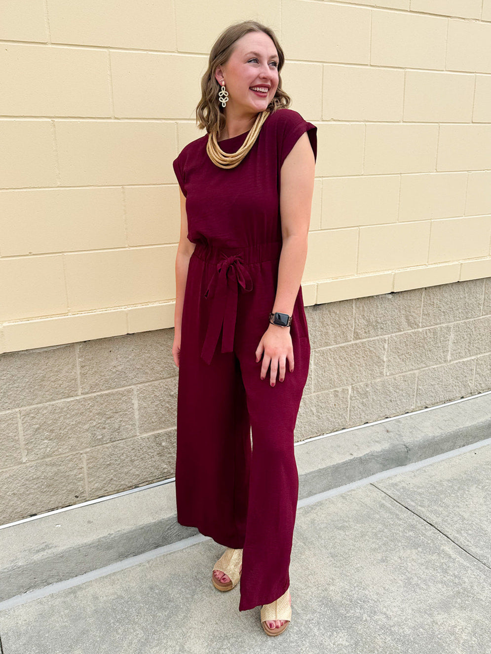 Garnet short-sleeve jumpsuit with elastic waist, front tie, high scoop neckline, and side pockets. Sporty, flattering, and perfect for Gameday style.