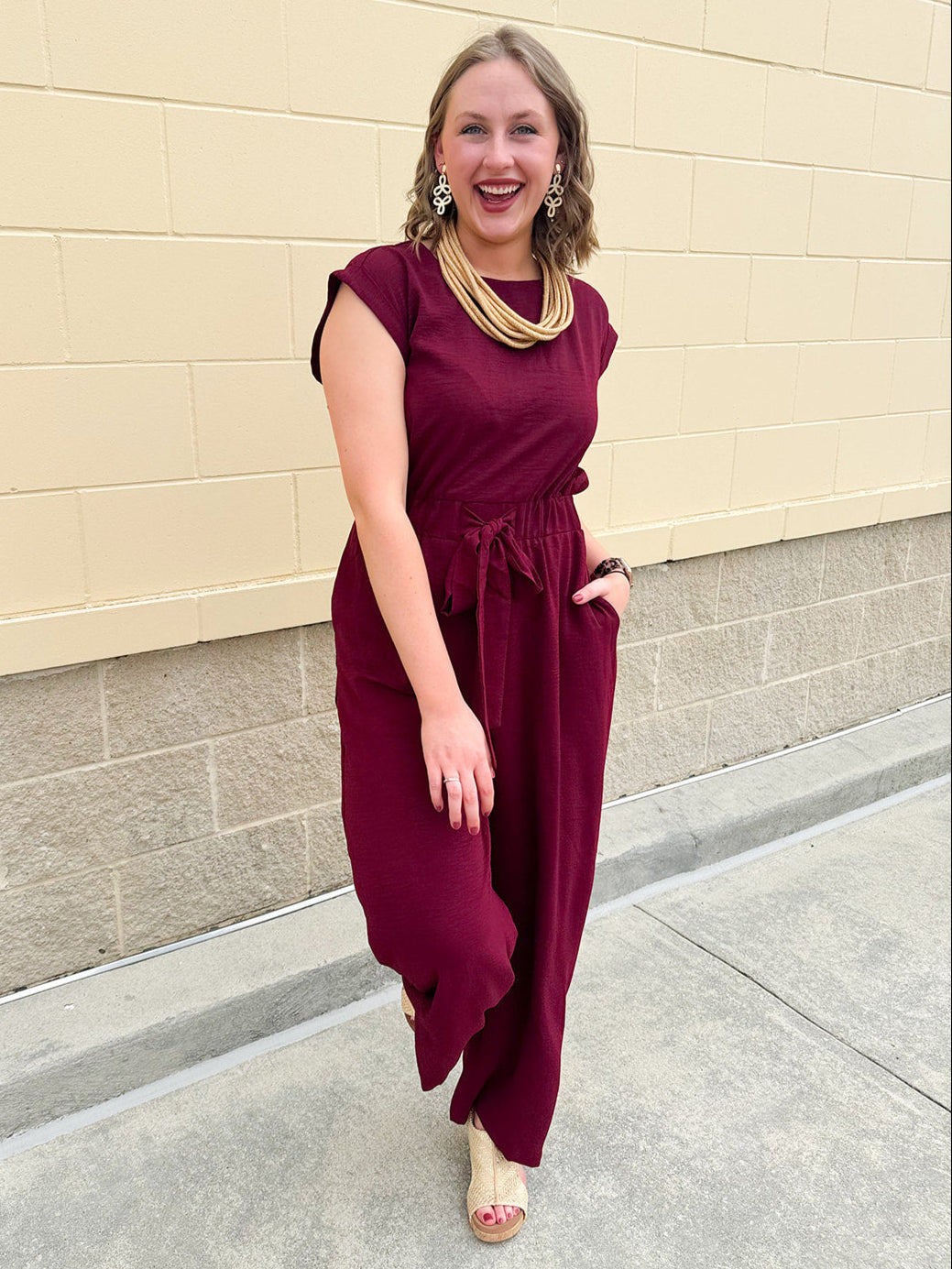 Garnet short-sleeve jumpsuit with elastic waist, front tie, high scoop neckline, and side pockets. Sporty, flattering, and perfect for Gameday style.