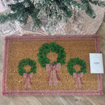 Christmas doormat with green wreaths, pink bows, and pink border.