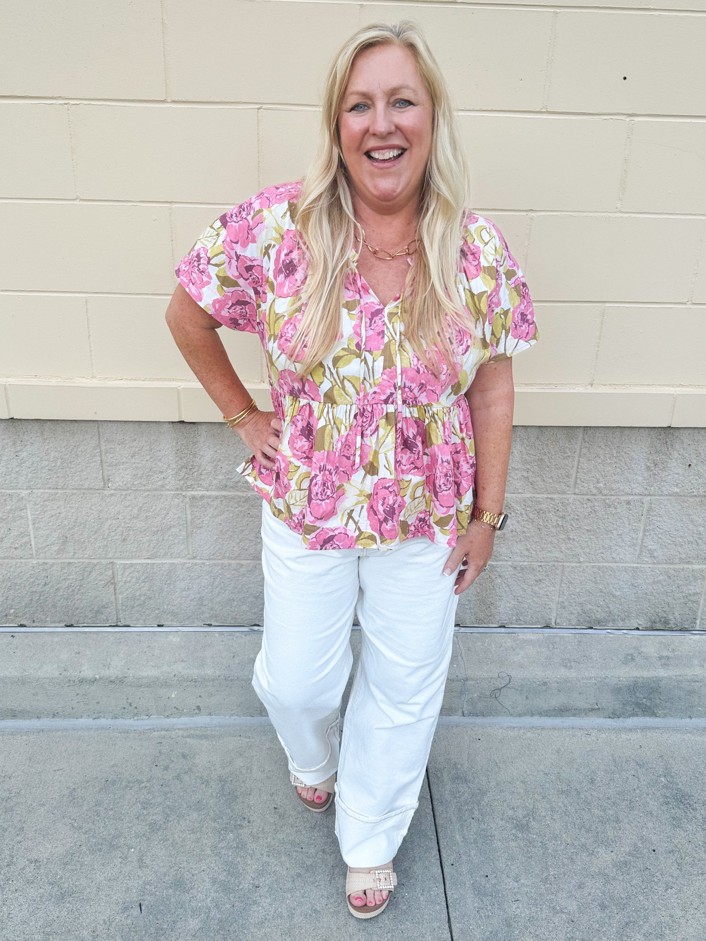 Pink floral babydoll top with ruffle collar, short sleeves, and a tie-neck detail, styled for a soft and feminine look.