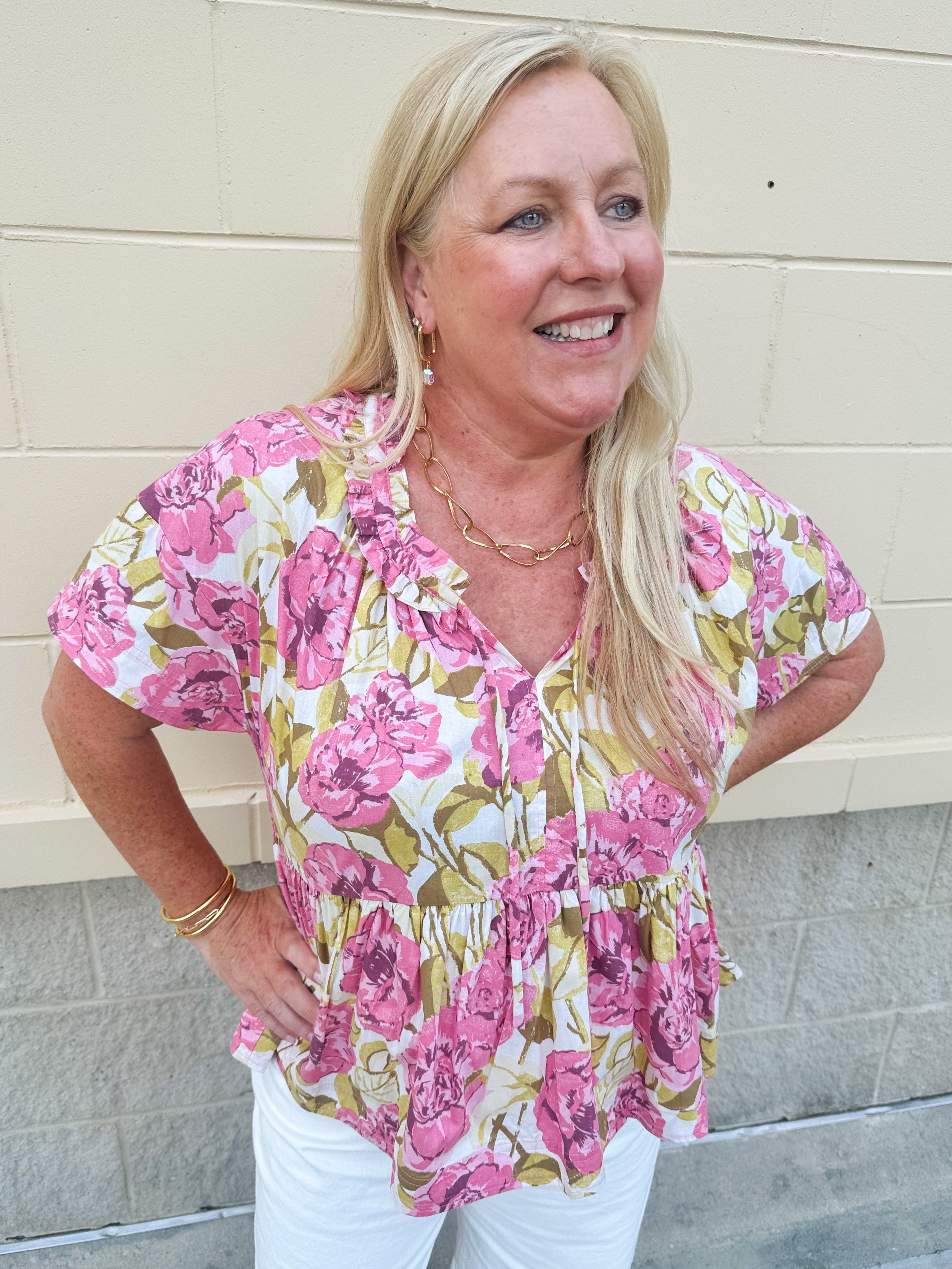 Pink floral babydoll top with ruffle collar, short sleeves, and a tie-neck detail, styled for a soft and feminine look.