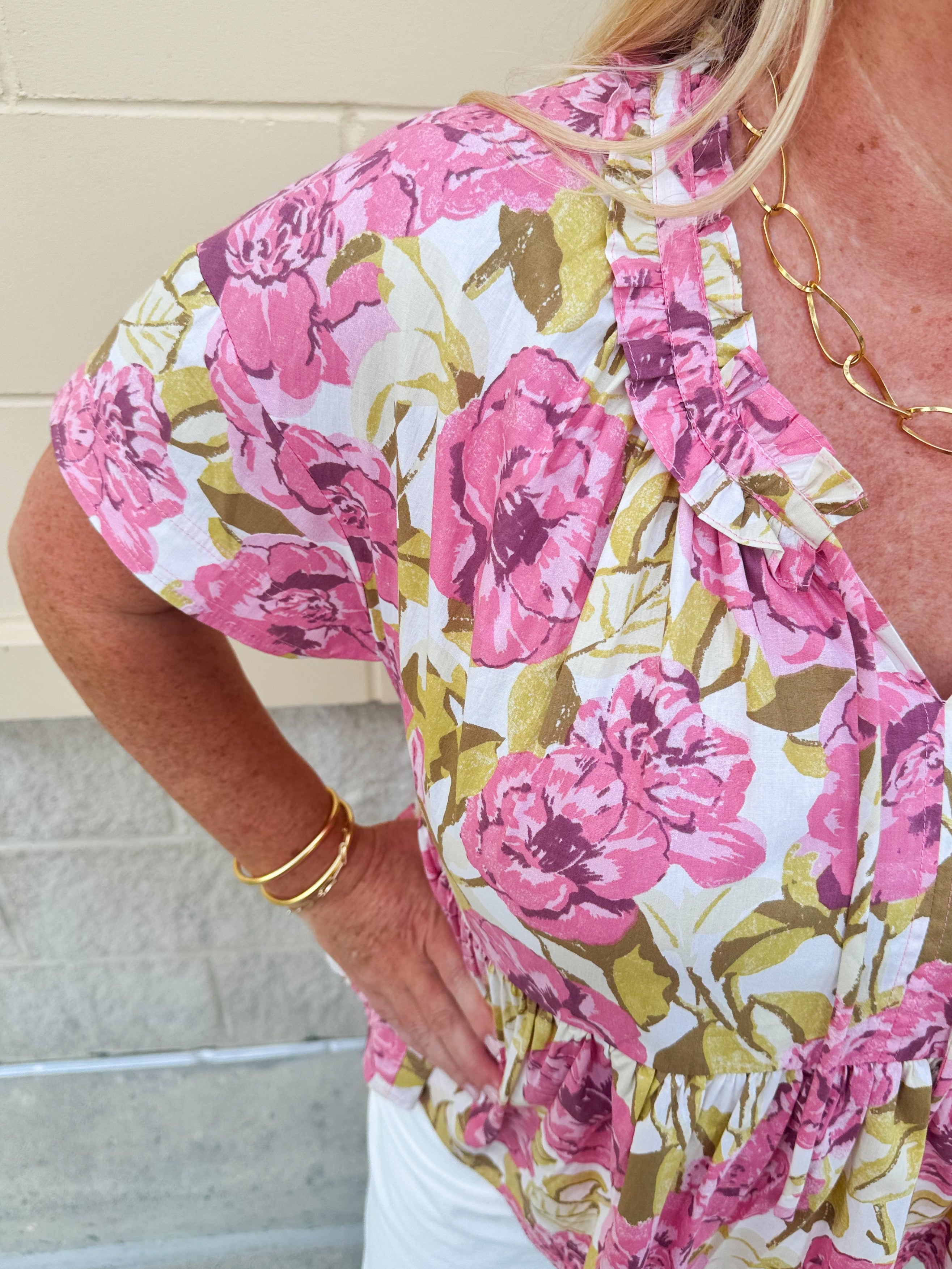 Pink floral babydoll top with ruffle collar, short sleeves, and a tie-neck detail, styled for a soft and feminine look.