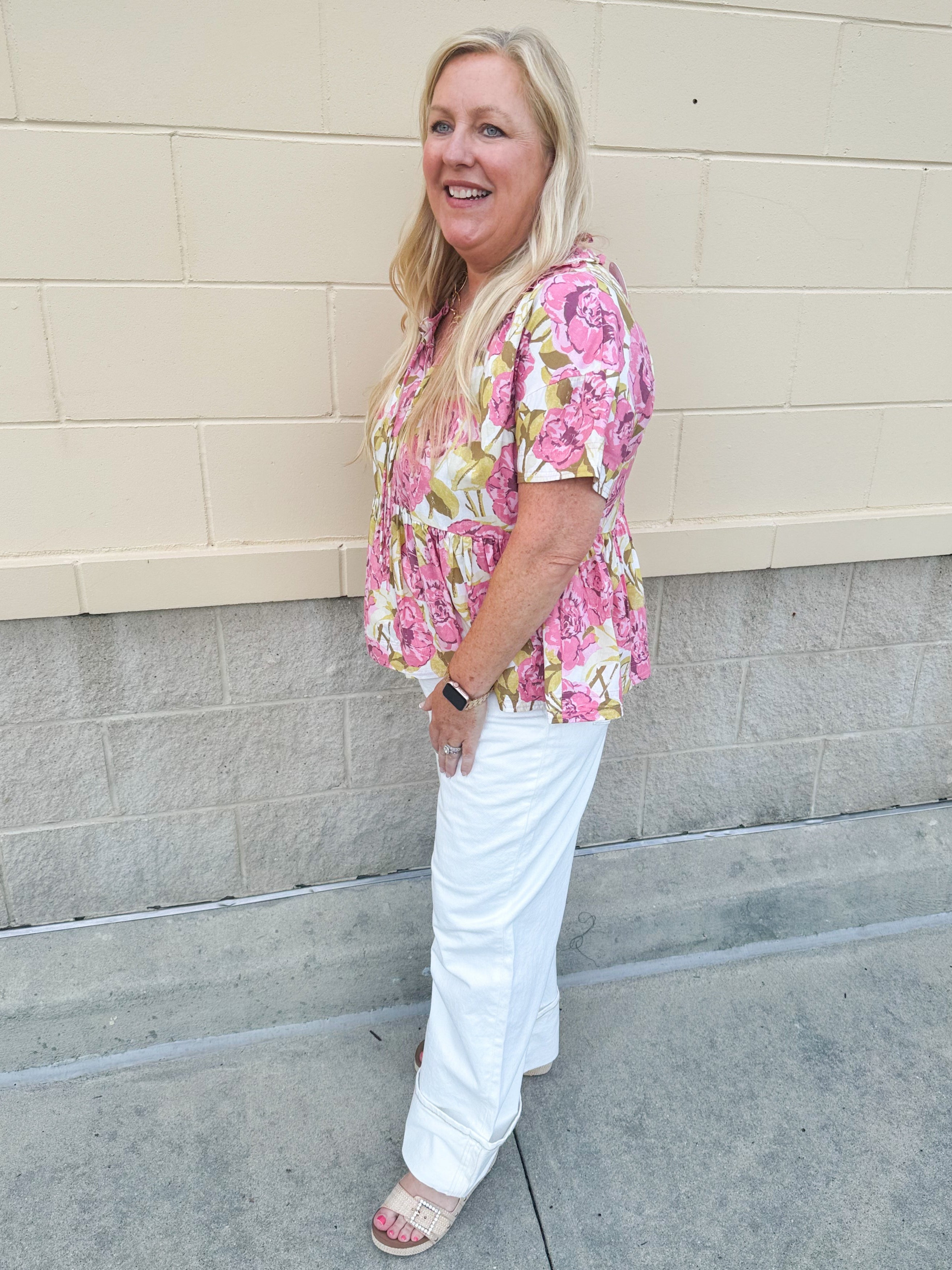 Pink floral babydoll top with ruffle collar, short sleeves, and a tie-neck detail, styled for a soft and feminine look.