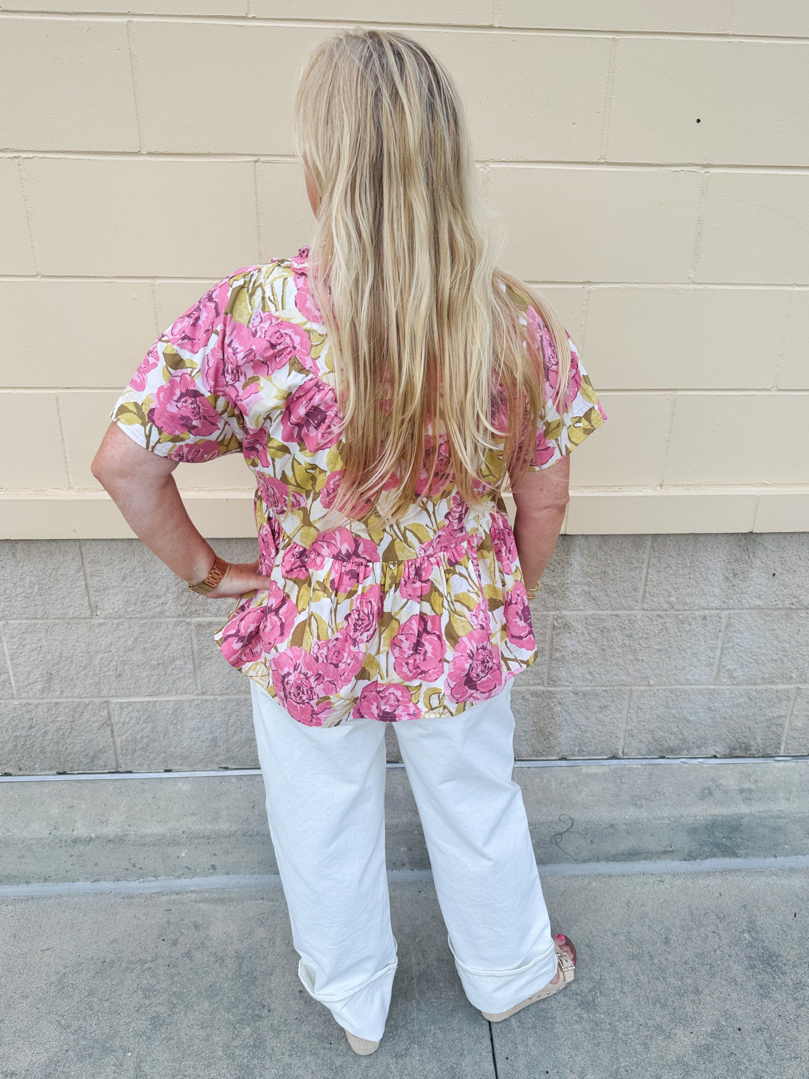 Pink floral babydoll top with ruffle collar, short sleeves, and a tie-neck detail, styled for a soft and feminine look.
