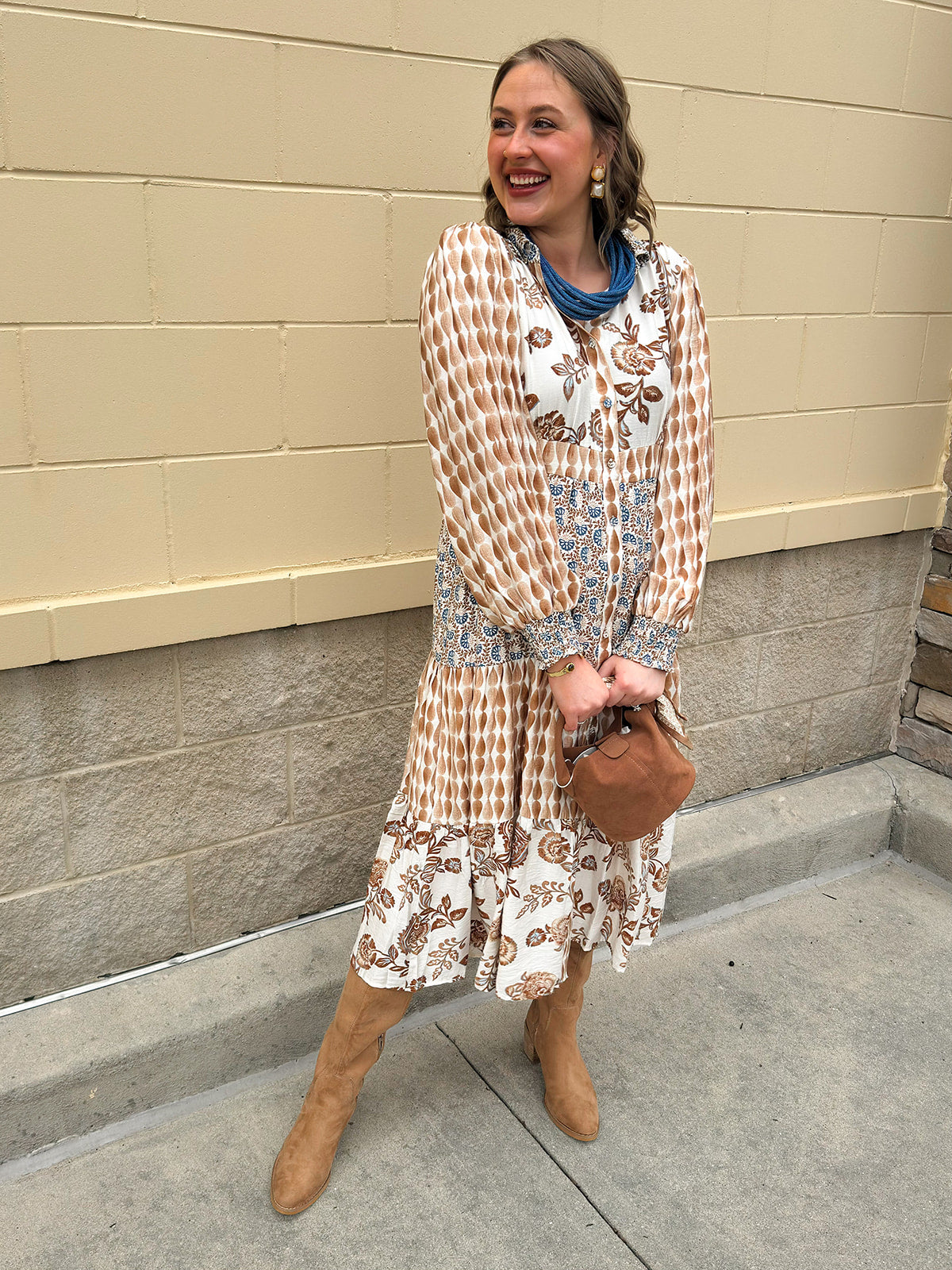 Tiered shirt dress in brown, cream, and blue mixed print with collared neckline, smocked details, and long sleeves.
