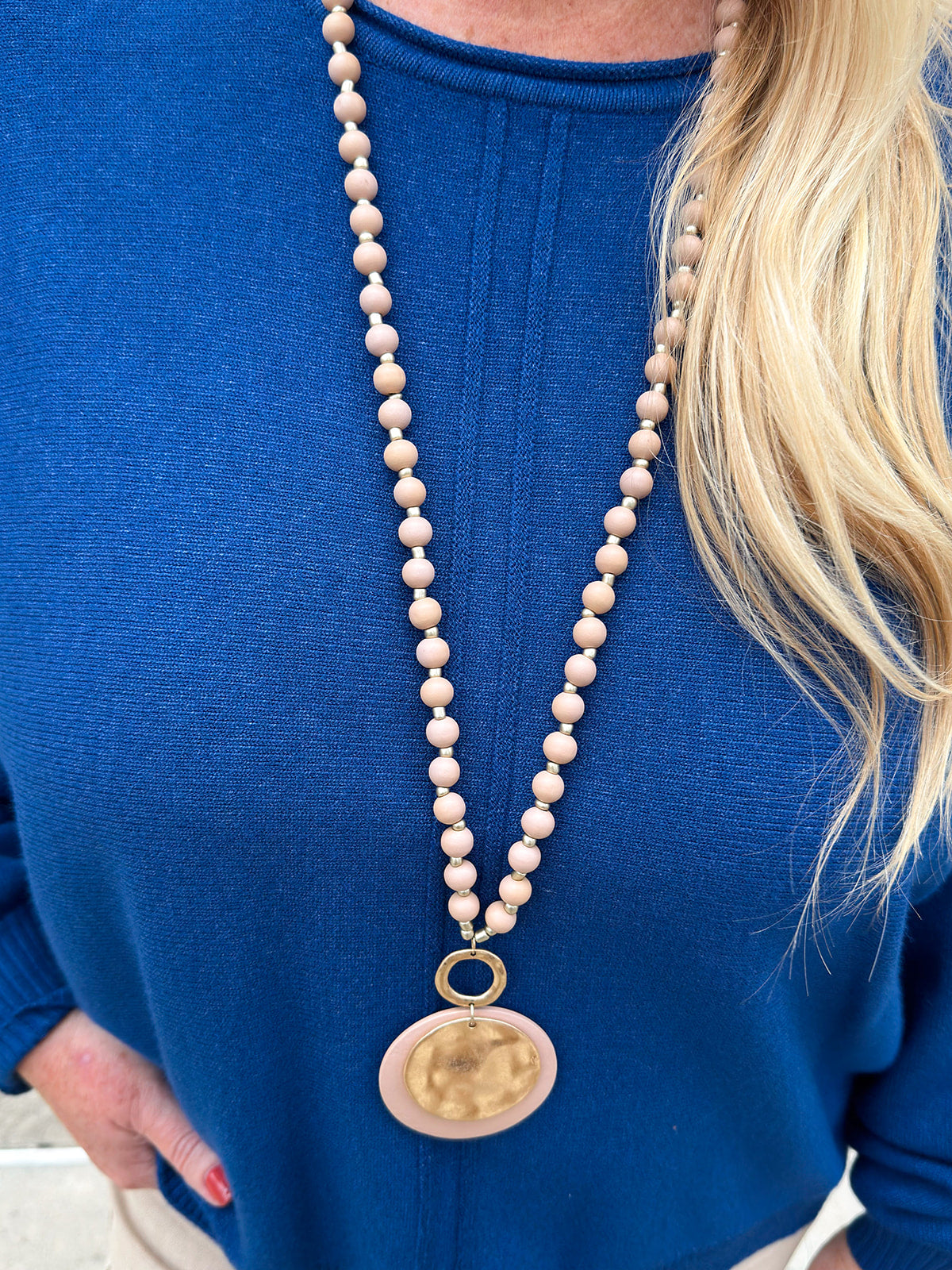 Tan beaded necklace with gold accents and a layered hammered gold and tan pendant, styled for versatile wear.