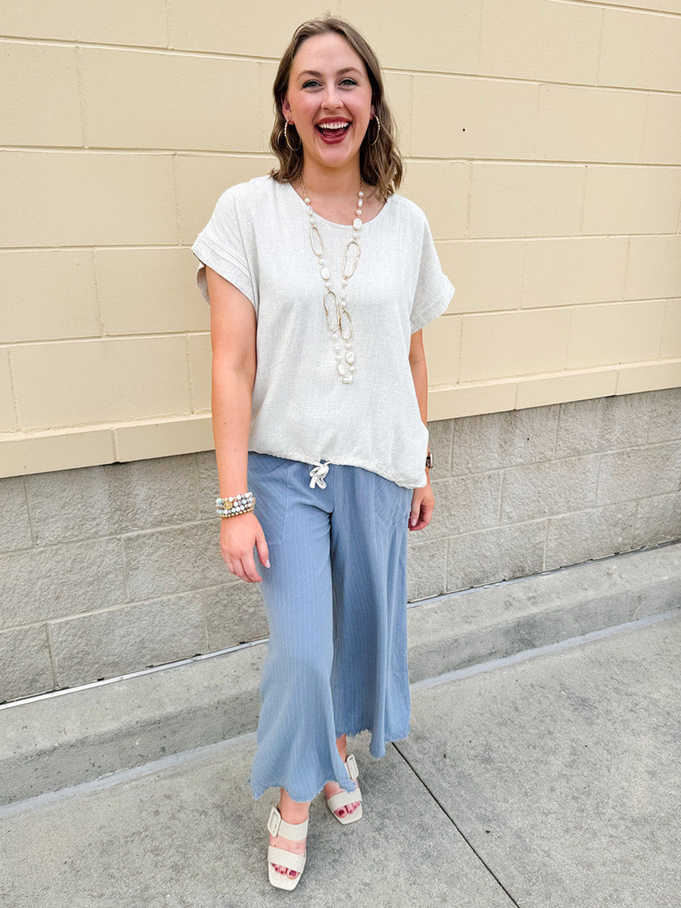Linen-cotton blend short-sleeve top with front tie and raw hem in a soft neutral oatmeal shade.