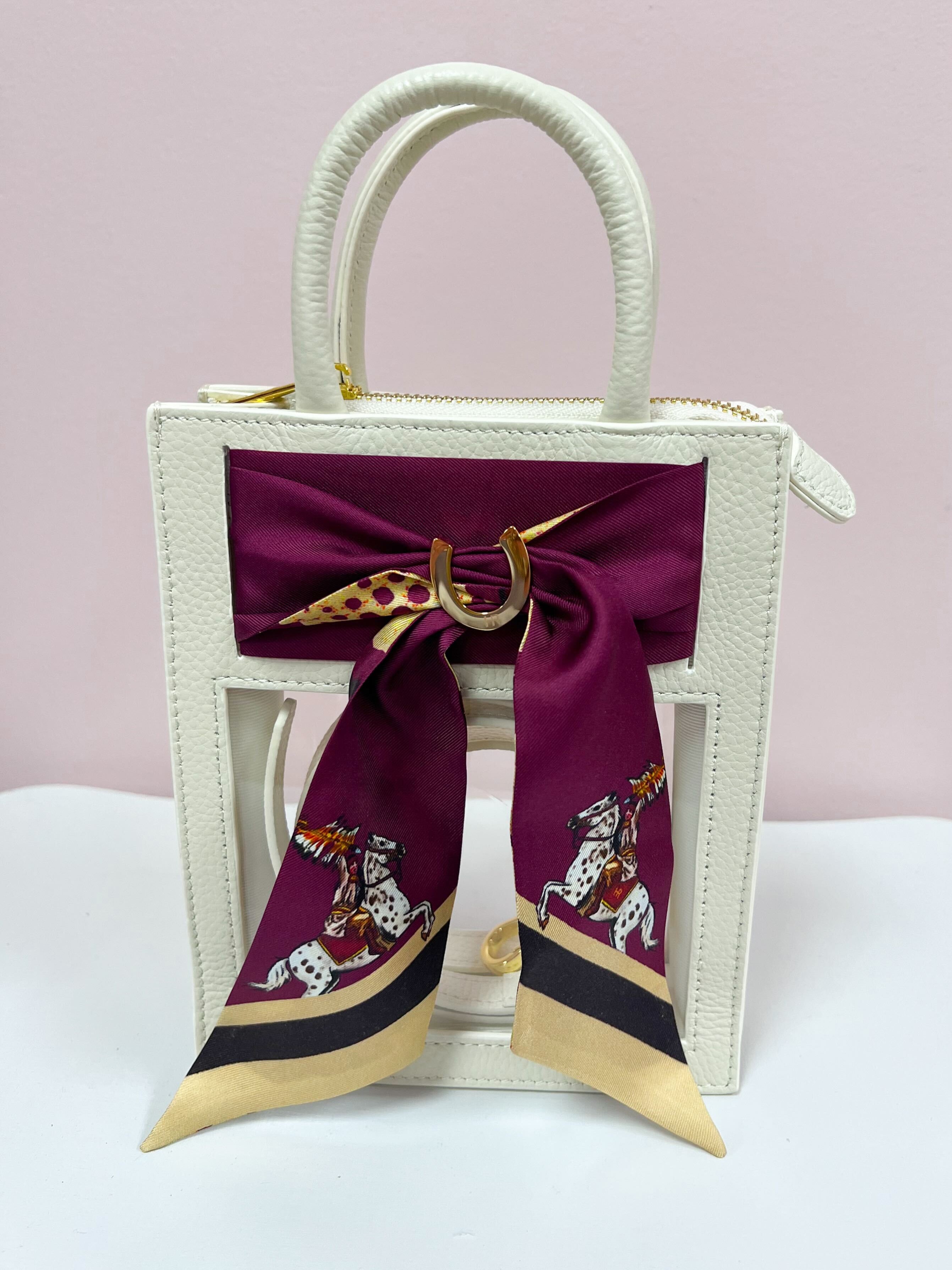Clear crossbody bag with cream leather trim, gold hardware, and a removable team scarf.