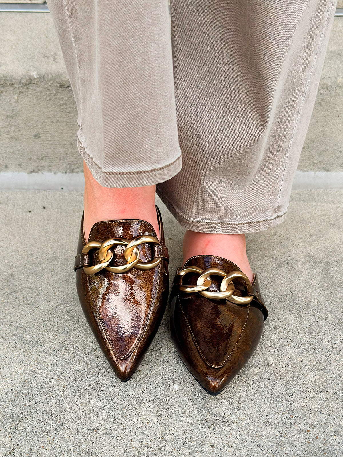 Bronze slip-on mules with glossy finish, gold chain detail, and pointed toe.