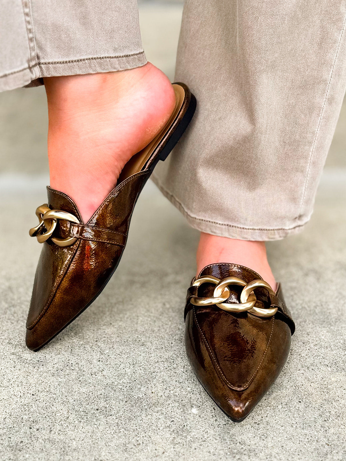 Bronze slip-on mules with glossy finish, gold chain detail, and pointed toe.