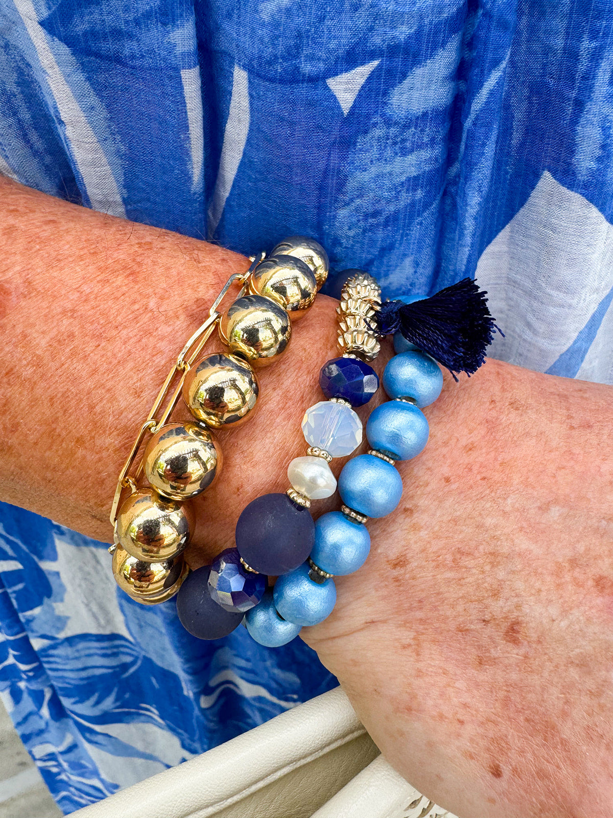 Layered charm bracelet stack featuring blue and gold glass beads, gold accents, and a tassel pendant for a stylish, boho-inspired look.