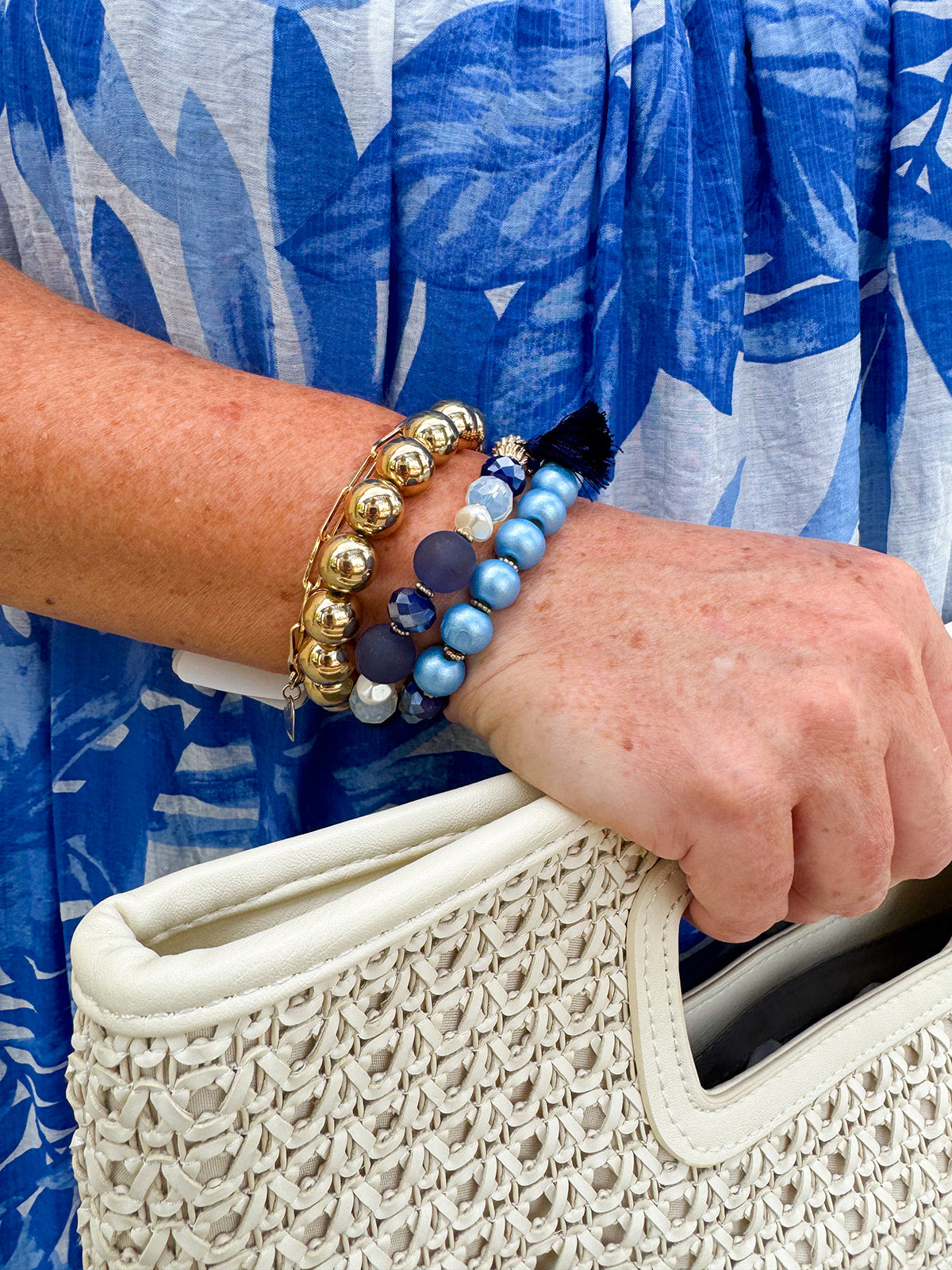 Layered charm bracelet stack featuring blue and gold glass beads, gold accents, and a tassel pendant for a stylish, boho-inspired look.