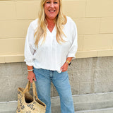 White V-neck loose-fit blouse with pleated cuffed sleeves, styled for a clean and classic outfit.