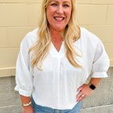 White V-neck loose-fit blouse with pleated cuffed sleeves, styled for a clean and classic outfit.
