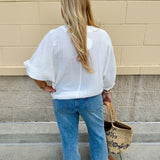 White V-neck loose-fit blouse with pleated cuffed sleeves, styled for a clean and classic outfit.
