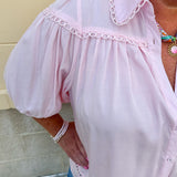 Solid pink button-down blouse with circular eyelet trim, ¾ sleeves, and pleated details, styled for a refined, feminine look.