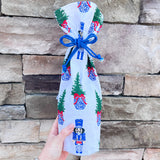 White bottle pouch with nutcracker and Christmas tree print, blue drawstring closure.