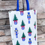 White wine caddy with nutcracker and Christmas tree print, blue handles.