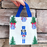White wine caddy with nutcracker and Christmas tree print, blue handles.