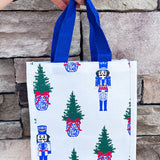 White compact tote with nutcracker and tree print and blue handles.