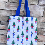 White everyday tote with nutcracker and Christmas tree print and blue handles.