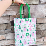 Tote bag with pink and green design held against a stone wall