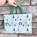 White rectangular market tote with pink and green holiday print featuring front doors, wreaths, potted trees, and green handles.