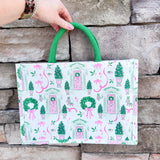 White rectangular market tote with pink and green holiday print featuring front doors, wreaths, potted trees, and green handles.