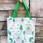 White compact tote with pink and green holiday print featuring front doors, wreaths, potted trees, and green handles.