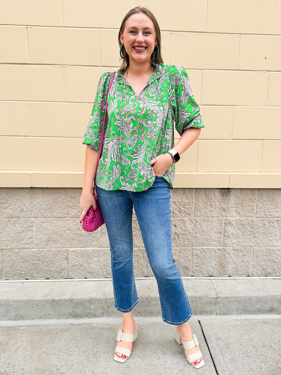 Green and pink paisley print blouse with frilled tie neckline and three-quarter peasant sleeves displayed on hanger against a neutral background