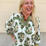 Cream floral blouse with olive and brown print, tassel ties, and decorative trim detailing.