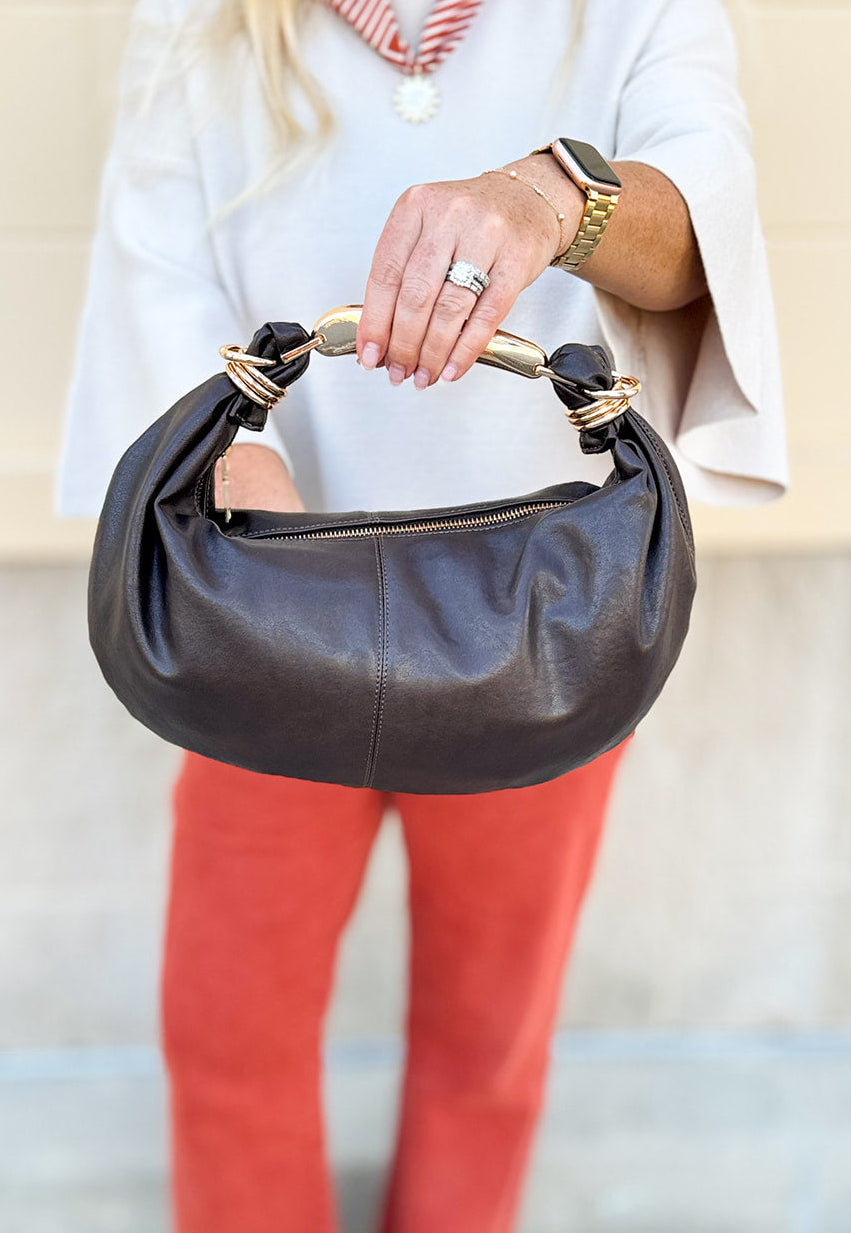 Chocolate brown asymmetrical pleather handbag with gold handle, gold hardware, and detachable crossbody strap.