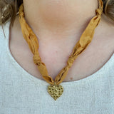 Gold scarf-style necklace with knotted details and hammered metal heart pendant.