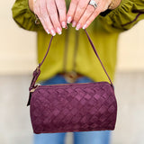 Plum-colored cylinder-shaped shoulder bag with adjustable buckle strap and zip closure.