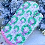 White oven mitt with green wreath and pink bow pattern, pink piping trim.