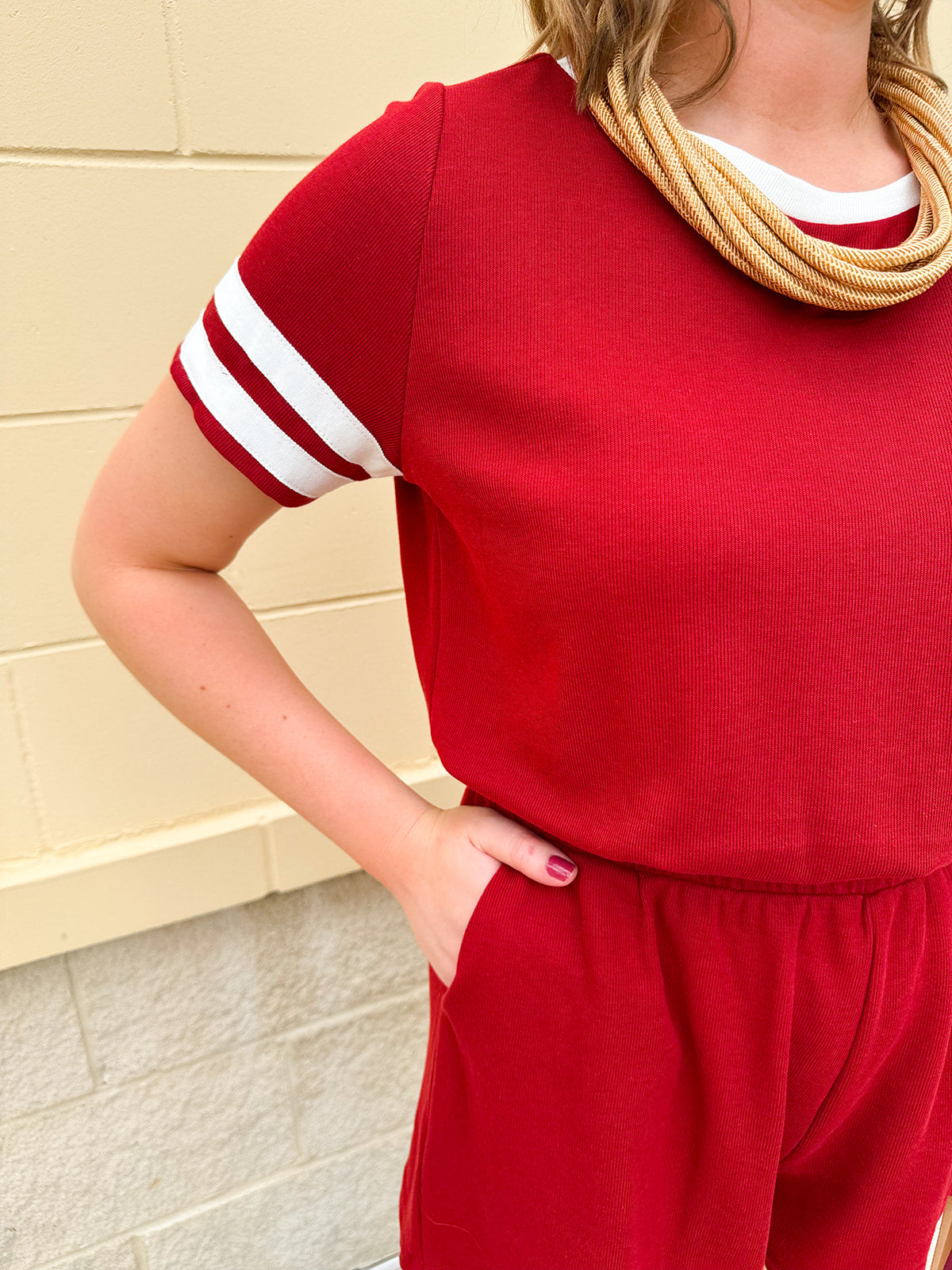 Garnet knit romper with white contrast trim on neckline, sleeves, and chest pocket. Features half sleeves, elastic waist, and keyhole back—sporty and stylish.