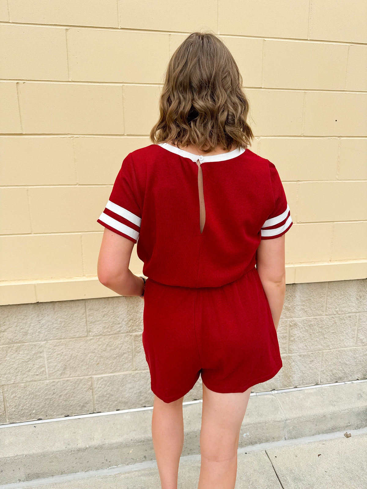 Garnet knit romper with white contrast trim on neckline, sleeves, and chest pocket. Features half sleeves, elastic waist, and keyhole back—sporty and stylish.