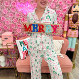 White pajama set with pink and green holiday house print, button-down top, and drawstring pants.
