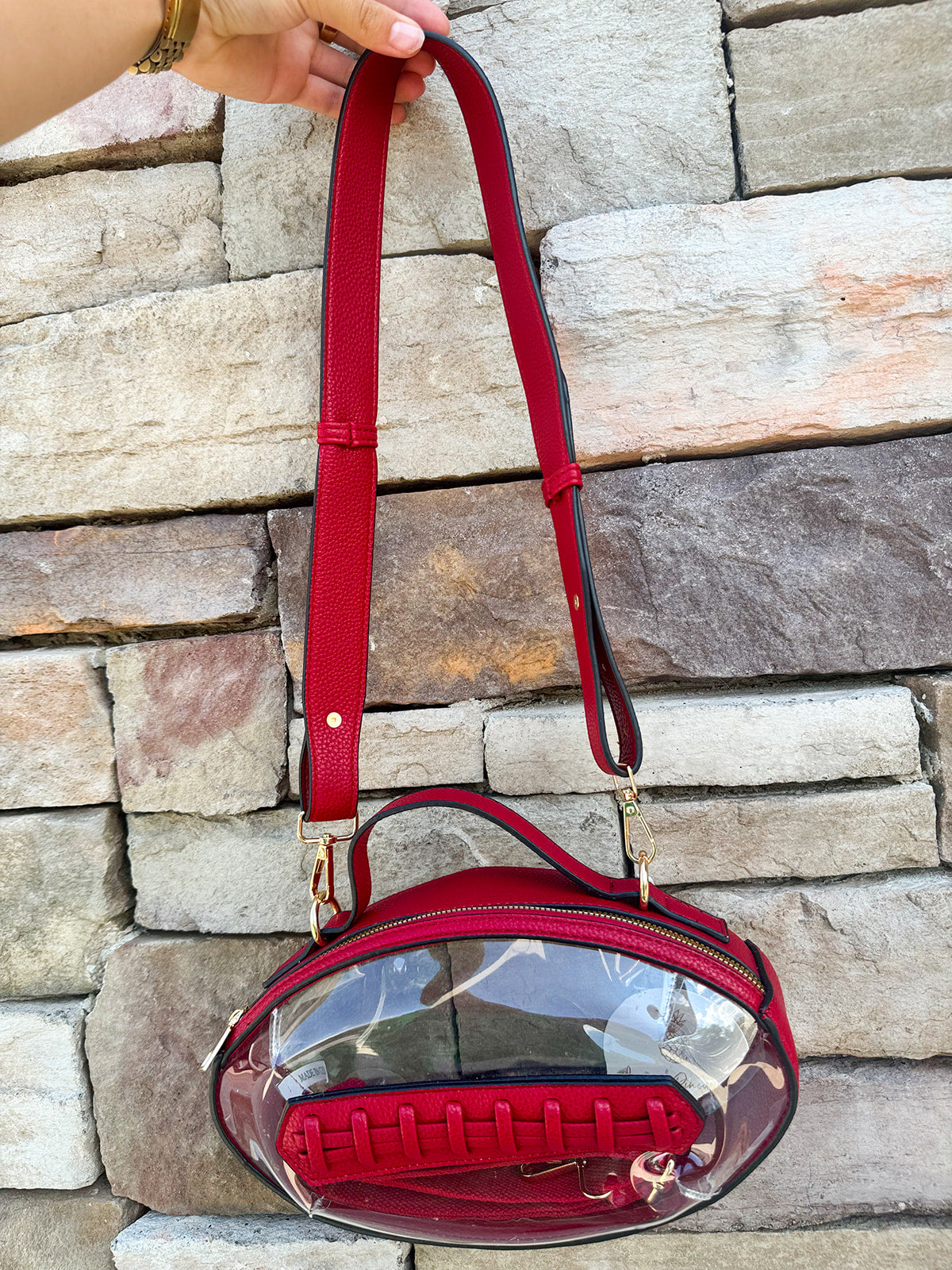 Clear football-shaped crossbody bag with garnet trim, zipper closure, and adjustable straps.